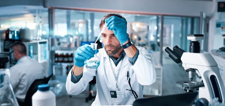 A pharmaceutical scientist in a lab coat and blue gloves using a pipette and a beaker in a modern pharmaceutical research facility